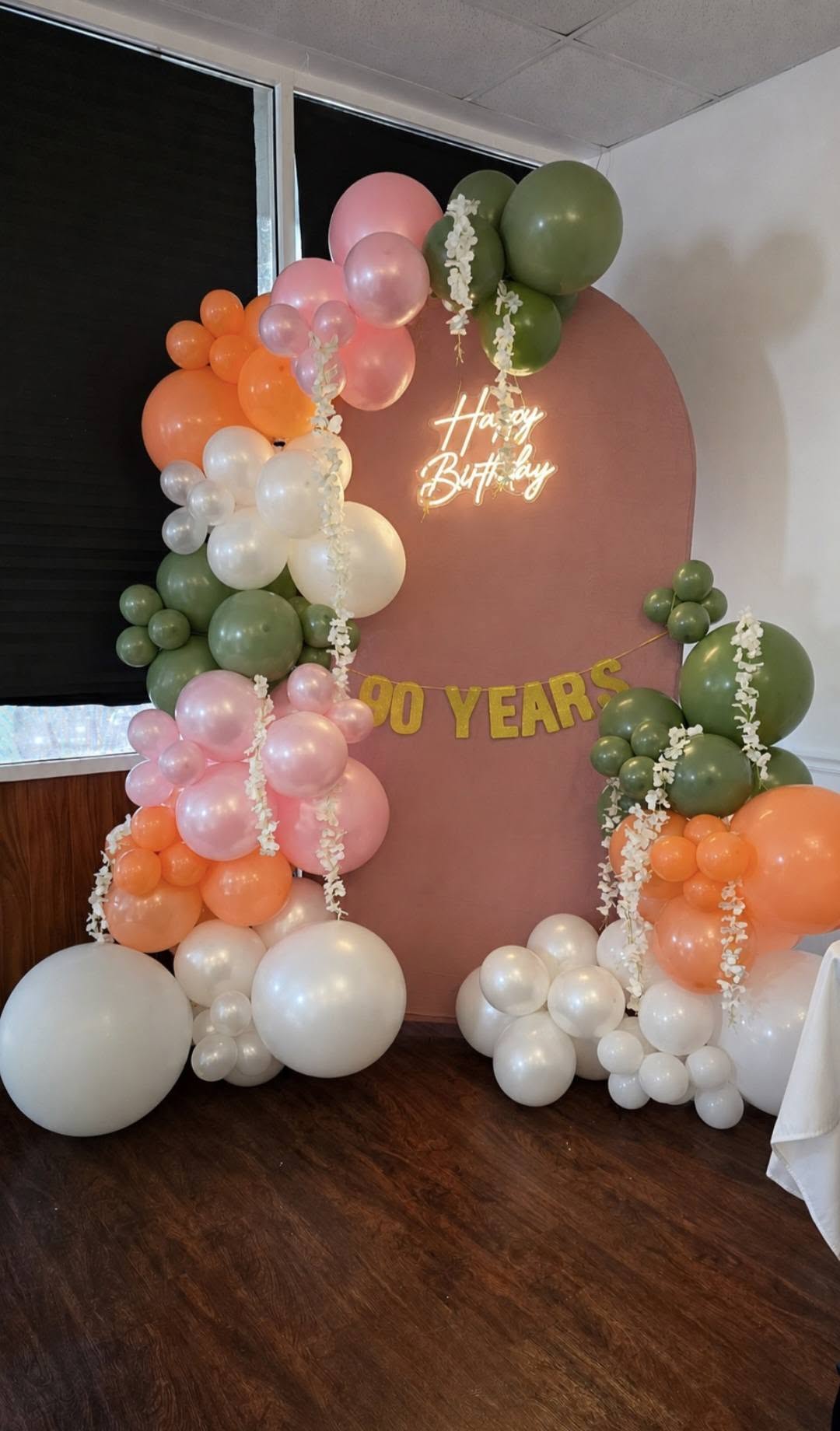 90th birthday balloon arch in sage, peach and pink with a Happy Birthday neon sign