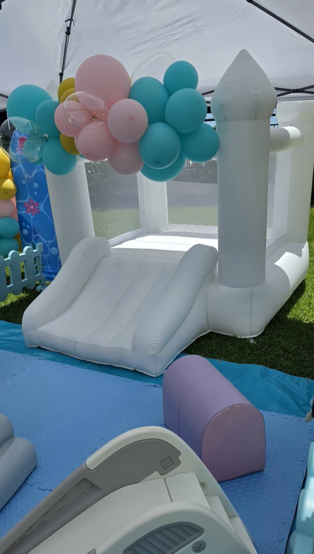 White bounce house with pastel balloon garland and soft play tunnels