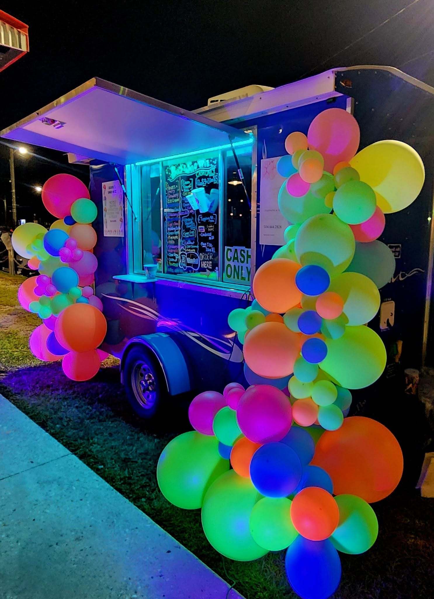 Glowing neon black-light balloon installation around a snowball stand at night