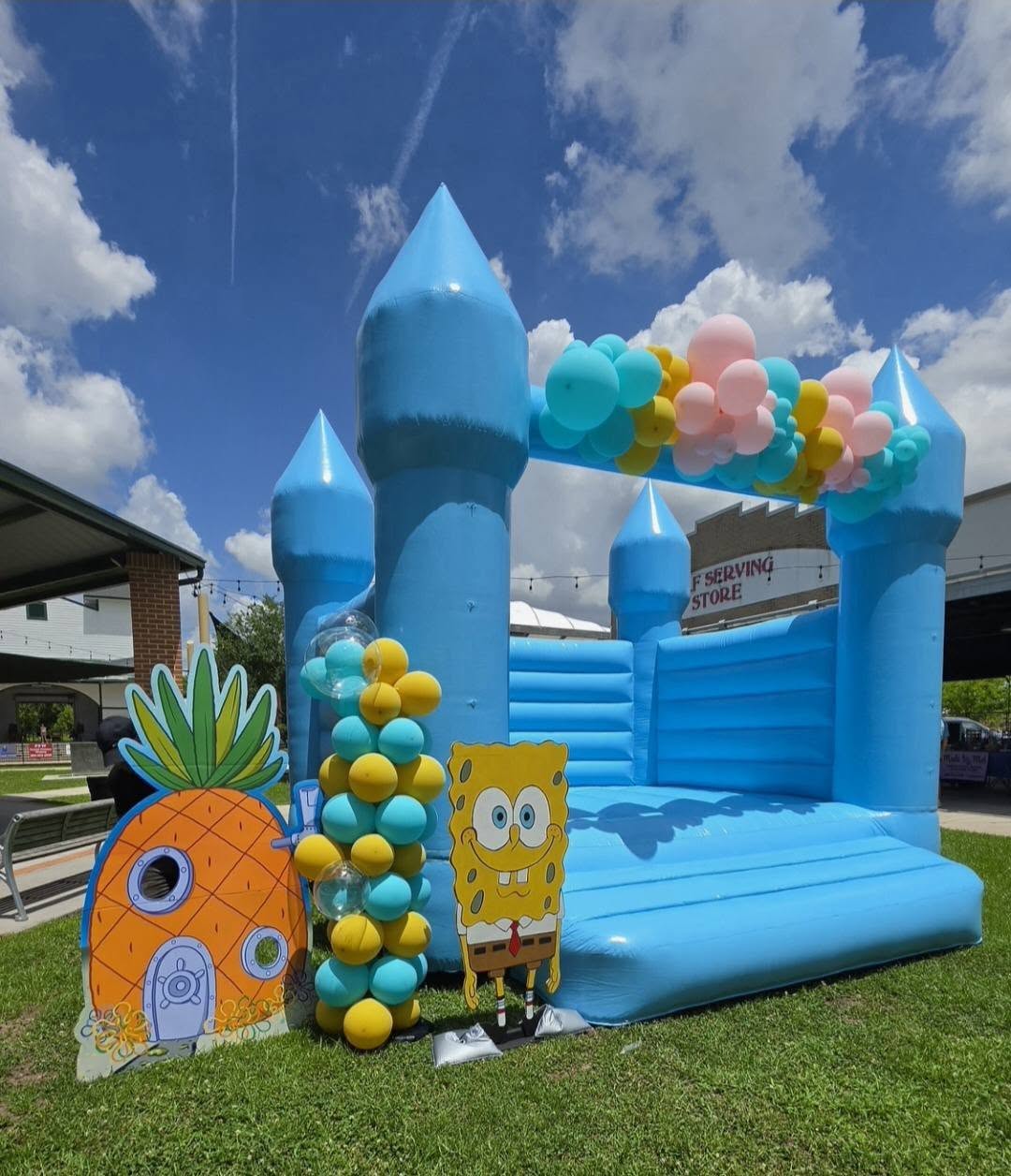 SpongeBob themed blue bounce castle with balloon column and character cutouts outdoors