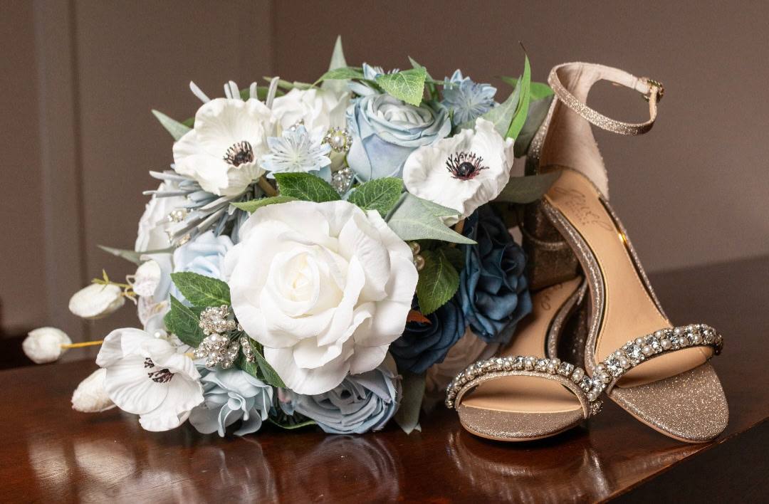 Bridal bouquet of white anemones and dusty blue roses beside crystal bridal heels