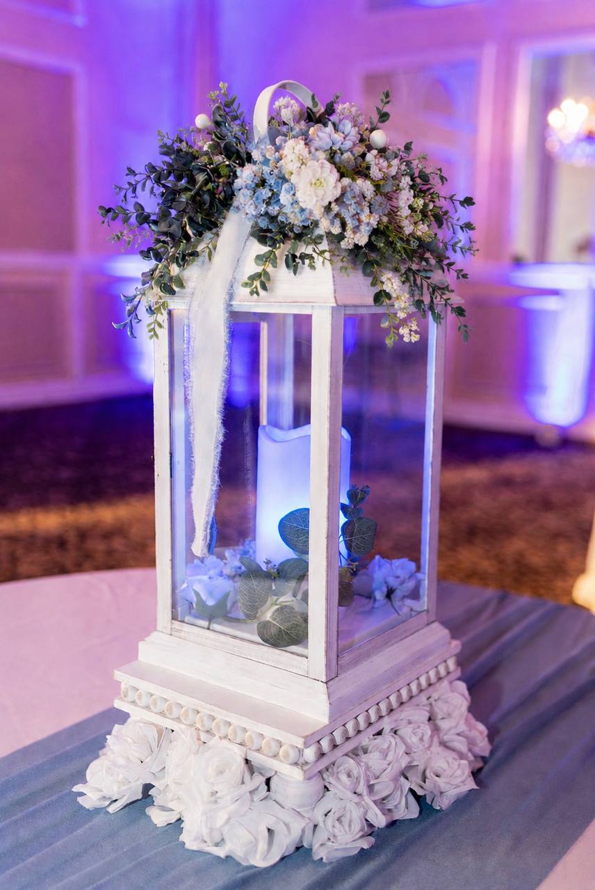 White lantern centerpiece topped with blue and ivory florals on a dusty blue linen